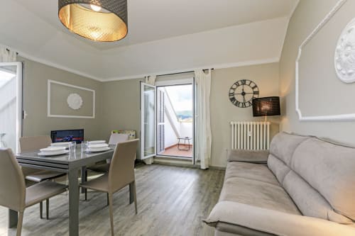 Moderno appartamento a Genova con divano beige, tavolo da pranzo, scrivania e accesso a balcone con vista sul mare