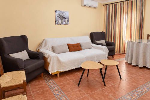 Acogedora sala de estar en Apartamentos Turísticos La Posada en Oropesa con sillones oscuros, sofá crema y mesitas de madera