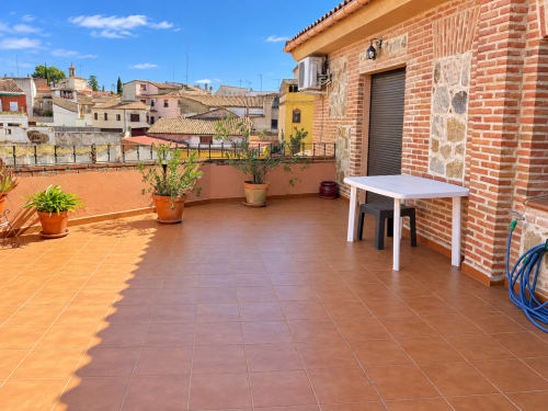 Soleada terraza de apartamento La Posada en Oropesa, Toledo, con suelo de barro cocido, plantas en macetas y vistas al pueblo