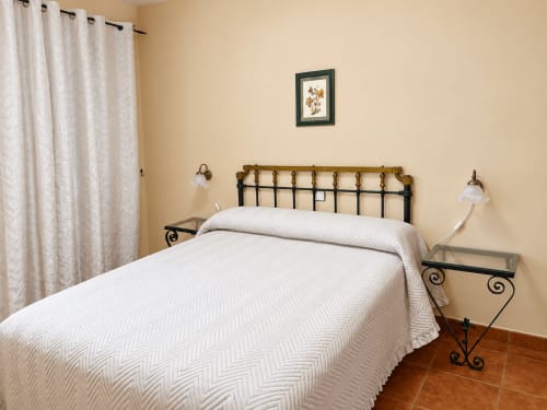 Habitación en apartamentos La Posada en Oropesa, Toledo con cama de hierro forjado, ropa de cama blanca y paredes color crema