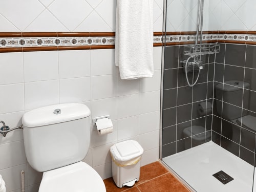 Baño moderno en Apartamentos La Posada, Oropesa. Azulejos blancos, ducha negra, inodoro, lavabo y toalla blanca.