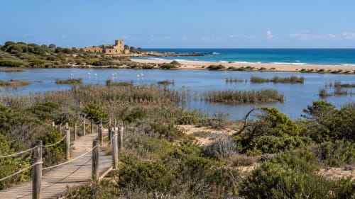 Passerella in legno attraverso la palude di Case Luparello, Noto, con vista sulla spiaggia, laguna e antica torre in pietra