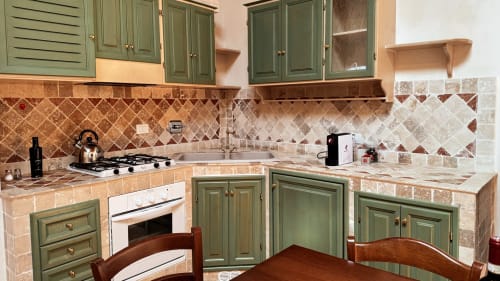 Borgo di Erboli apartment kitchen with green cabinets, tiled counters, gas stove, and backsplash in Cavriglia.