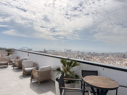 Terraza en azotea de Sinese Design Homes en Málaga con sillas de mimbre, mesa de comedor y vistas panorámicas de la ciudad