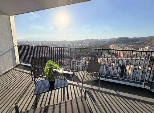 Balcón de apartamento en Málaga con vistas a las montañas, zona de estar y horizonte de la ciudad bajo la luz del sol