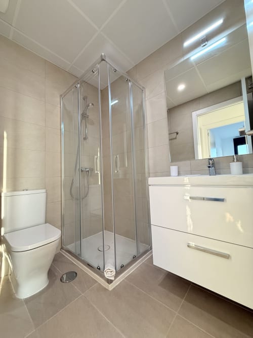 Cuarto de baño moderno en apartamento de Málaga con mampara de ducha esquinera, lavabo blanco, inodoro y suelos radiantes