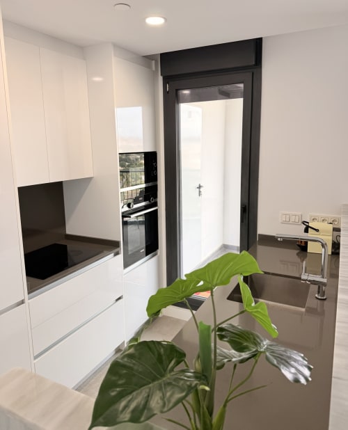 Cocina moderna en apartamento Martiricos, Málaga con muebles blancos, encimera negra, electrodomésticos acero inoxidable