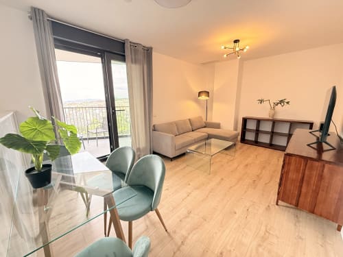 Moderno salón de apartamento en Málaga con vistas a la montaña, sofá beige, mesa de comedor, cocina americana y acceso a balcón
