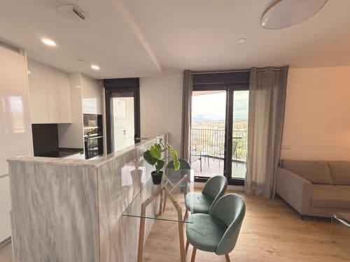 Moderno salón de apartamento en Málaga con cocina, mesa de comedor, sillas verdes y vistas a las montañas desde el balcón