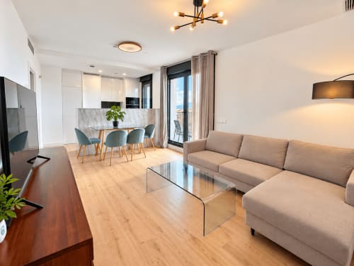 Moderno apartamento en Málaga con salón diáfano, sofá beige, comedor y vistas a la montaña desde el balcón