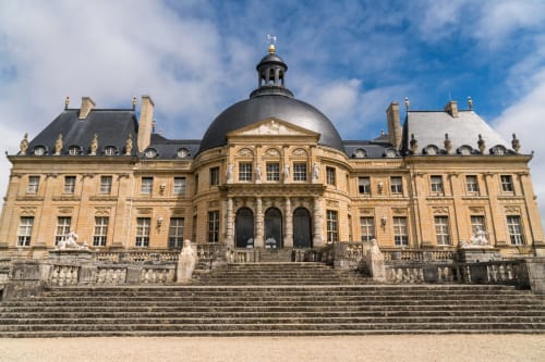 Grand château classique aux façades dorées et dôme majestueux, avec jardins soignés et architecture formelle