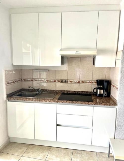 Modern studio kitchenette in Costa Adeje, Tenerife with white cabinetry, granite countertop, and stainless steel appliances