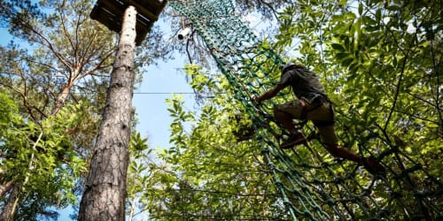 Client parcourant un sentier acrobatique en forêt au parc aventure de l'Hôtel Motelia, Moissy-Cramayel