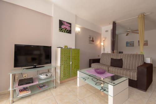 Modern studio apartment in Costa Adeje with striped sofa, flat-screen TV, glass coffee table, and green storage unit
