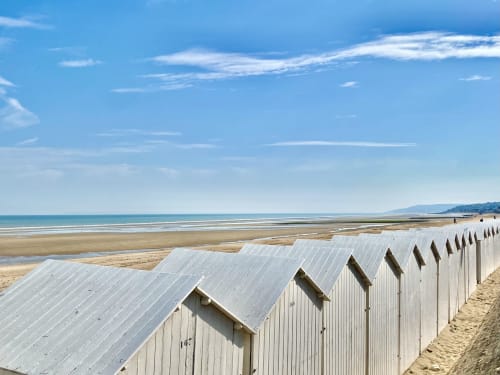 Rangée de cabines de plage blanches sur le sable avec mer turquoise et ciel bleu aux Plages Normandes, Normandie