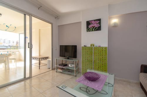 Modern studio apartment living area in Costa Adeje with TV, green storage units, purple accents, and balcony access