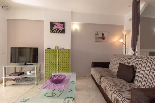 Modern studio living room in Costa Adeje with striped sofa, flat-screen TV, green storage units, and contemporary décor