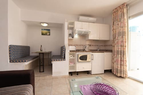 Modern studio apartment kitchen and dining area in Costa Adeje with white cabinetry, microwave, and seating nook with pool