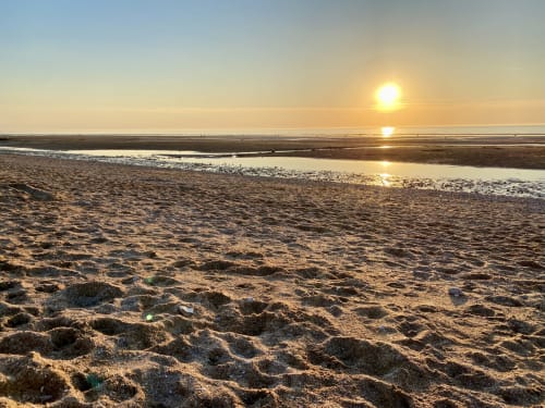 Coucher de soleil doré sur la plage de sable avec bassins de marée aux Roches de Normandie
