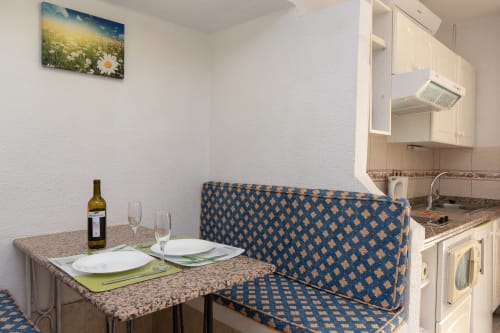 Modern studio apartment in Costa Adeje featuring dining area with blue patterned sofa, kitchen, and place settings with wine