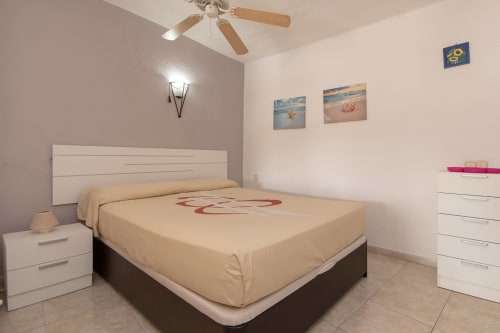 Modern studio bedroom in Costa Adeje with queen bed, white headboard, ceiling fan, and ocean-themed artwork