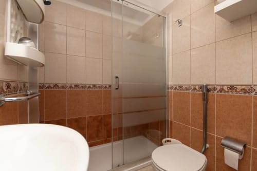Modern bathroom with beige and terracotta tiles, glass shower enclosure, white toilet and sink in Costa Adeje apartment