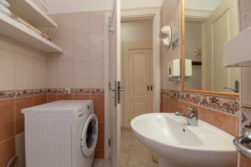 Modern bathroom in Costa Adeje studio with washing machine, white sink, mirror, and terracotta tile accents