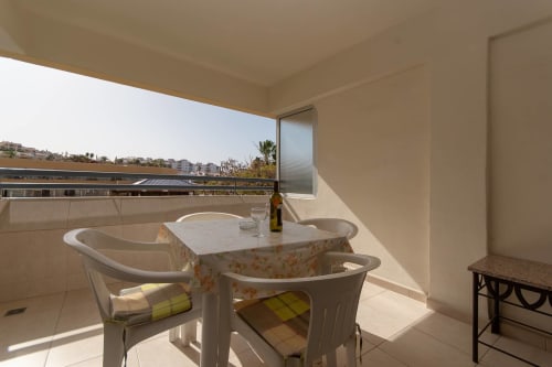 Sunny balcony with dining table and chairs overlooking Costa Adeje, Tenerife with pool views and distant cityscape