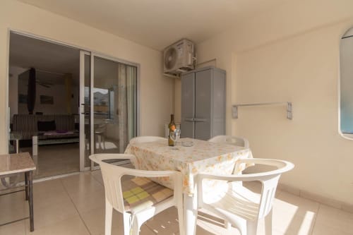 Bright balcony dining area with white chairs and floral tablecloth overlooking Costa Adeje, Tenerife, with AC unit and pool