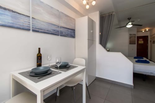 Modern studio apartment dining area with set table, wine bottle, and bedroom visible in Costa Adeje, Tenerife