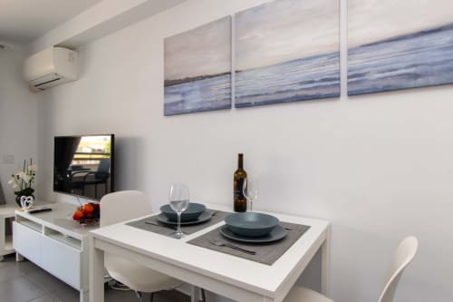 Modern studio dining area with set table, wine bottle, TV, and coastal-themed wall art in Costa Adeje apartment