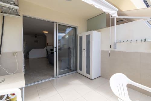 Studio apartment patio with sliding glass doors opening to bedroom, beige tiling, white furniture, and sea views in Costa