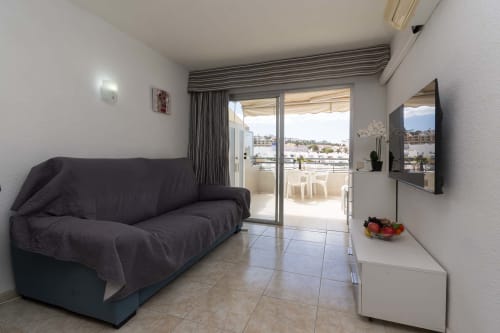 Modern studio apartment living room in Costa Adeje, Tenerife with sea view balcony, dark sofa, flat-screen TV, and terrace