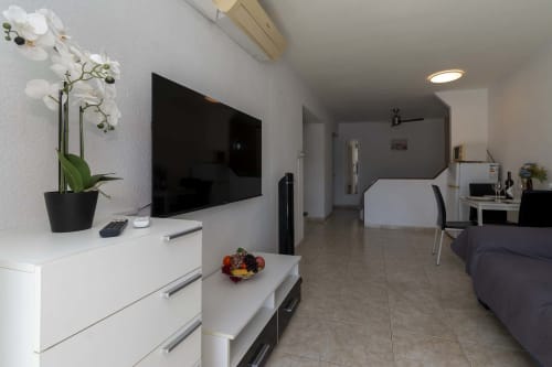 Modern studio apartment in Costa Adeje with living area, TV, white furniture, orchid plant, and dining space