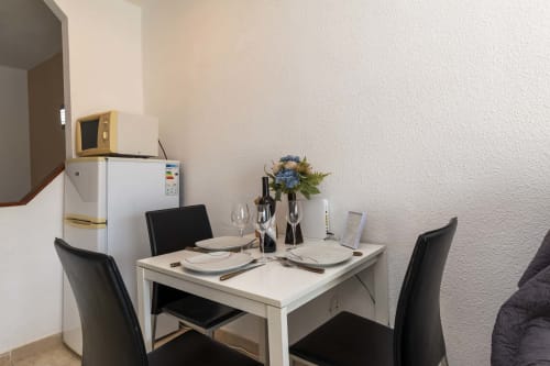 Modern dining area in Studio Apartment with white table, black chairs, place settings, flowers, microwave and refrigerator in