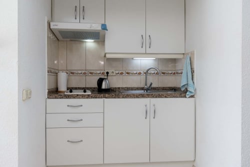 Compact kitchenette in Costa Adeje studio apartment with white cabinets, granite countertop, and modern appliances