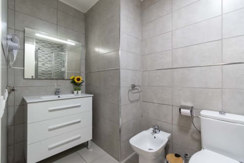 Modern bathroom in Costa Adeje studio apartment with white vanity, tiled shower enclosure, bidet, and illuminated mirror