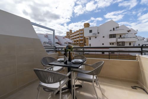 Modern balcony with outdoor dining table and chairs overlooking Costa Adeje, Tenerife buildings and blue sky
