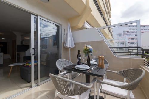 Modern balcony dining area at Costa Adeje apartment with table, chairs, wine, and sea views