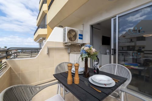 Balcony dining area at Costa Adeje apartment with set table, flowers, ocean view, and Haier AC unit