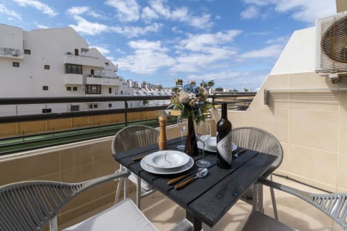 Balcony dining setup at Costa Adeje apartment with table, chairs, wine, and city views