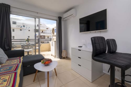 Modern studio apartment in Costa Adeje, Tenerife with black seating, white furniture, flat-screen TV, and balcony overlooking