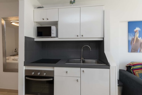 Modern studio apartment kitchenette in Costa Adeje with white cabinets, black countertop, microwave, cooker, and sink