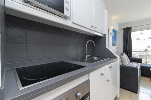 Modern studio kitchen with black backtile, white cabinetry, induction cooktop, and sink in Costa Adeje apartment