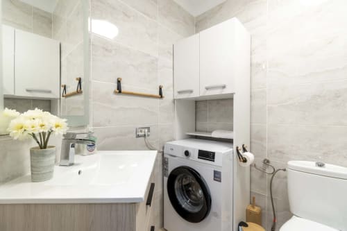 Modern studio apartment bathroom in Costa Adeje with marble tiles, sink, washing machine, and toilet