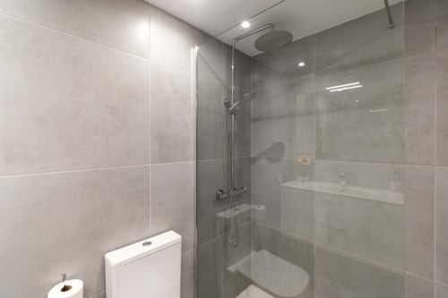 Modern bathroom with walk-in shower, glass enclosure, and grey tile walls in Costa Adeje studio apartment