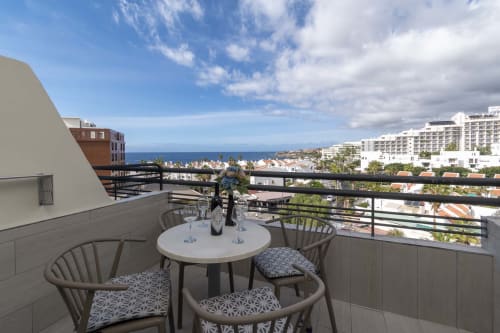 Balcony terrace at Costa Adeje hotel with sea views, round table, chairs, and ocean horizon beyond residential buildings.