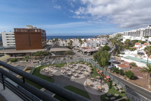 Aerial view of Costa Adeje resort with sea-facing courtyard, palm trees, pools, and Mediterranean architecture in Tenerife