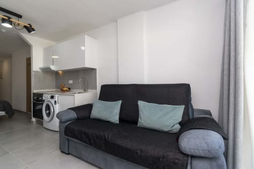 Modern studio apartment in Costa Adeje with black sofa, light pillows, kitchenette, washing machine, and contemporary