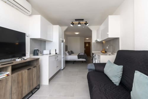 Modern studio apartment in Costa Adeje with kitchenette, living area with black sofa, TV, and bed visible in background